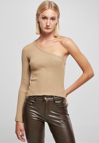 Beige bordás kötött top, egy vállas, testhez simuló kialakítással és cropped szegéllyel. Barna, magas derekú műbőr nadrággal párosítva.