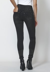 Svarta smala jeans med horisontell ribbning vid midjan och nitar vid fotleden. Har två bakfickor.