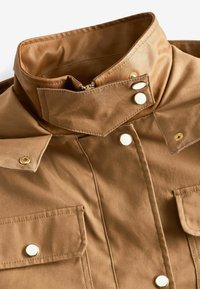 Veste marron avec col haut, boutons-pression, poches à rabat à l'avant et fermeture à glissière sous le col.