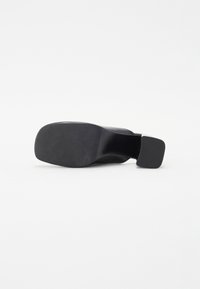 Scarpa nera con tacco quadrato, tomaia in pelle liscia e suola testurizzata. Design semplice, accenti minimi e silhouette slanciata.