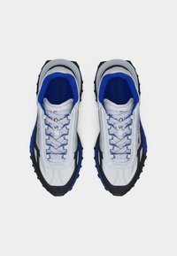 Ζευγάρι αθλητικών παπουτσιών Lacoste σε λευκό, μαύρο και μπλε χρώμα με κορδόνια, απεικονιζόμενα από πάνω σε λευκό φόντο.