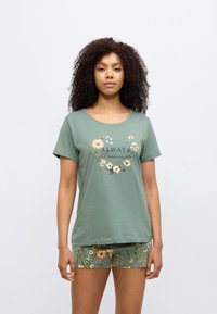 Πράσινο βαμβακερό T-shirt με λουλουδάτο σχέδιο και το κείμενο «ALWAYS blooming.» Συνδυασμένο με σορτς με παρόμοιο λουλουδάτο μοτίβο. Με κοντά μανίκια.