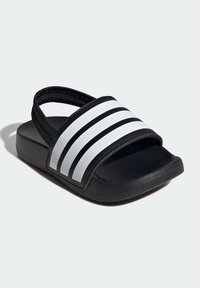 Mustat liukupohjaiset sandalsit, joissa on kolme valkoista vaakasuoraa raitaa. Valmistettu synteettisestä materiaalista, jossa on teksturoitu pohja ja pehmustettu pohjallinen.