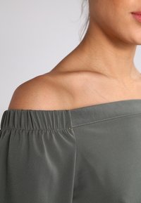 Off-the-shoulder top in donkergrijs, gemaakt van soepele stof. Heeft een geplooide rand langs de halslijn en een ontspannen pasvorm.