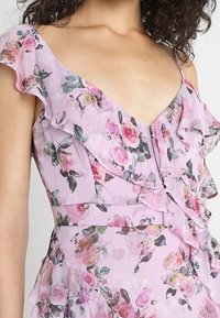 Blomsterklänning i ljuslila med volangärmar, prydd med rosa rosor och gröna blad. Lätt tyg med en djup V-ringning.