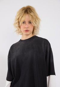 Übergroßes schwarzes T-Shirt mit kurzen Ärmeln, weichem Material, Rundhalsausschnitt, dezentem Glanz und kontrastierendem weißen Stoff an den Bündchen.