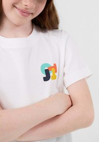 Witte katoenen t-shirt met een multikleurig grafisch logo op de borst met vormen in blauw, oranje, geel en teal. Korte mouwen.