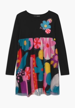 Czarna długa sukienka z długim rękawem, ozdobiona dużymi kolorowymi kwiatowymi wzorami na spódnicy i klatce piersiowej, z tekstem "Bądź sobą" zintegrowanym w projekcie.