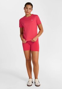 Pink t-shirt med korte ærmer og et lille logo på brystet, kombineret med matchende shorts. Stoffet ser glat ud med et tætsiddende design.