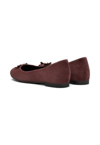 Ballerines en suede bordeaux avec un bout arrondi et un petit nœud décoratif. Semelle noire plate, texture douce et design simple.