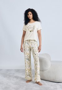 Σετ πιτζάμας από κρεμ βαμβάκι με κοντομάνικη μπλούζα με λουλουδένιο σχέδιο και παντελόνι με φαρδιά μπατζάκια και κίτρινα και πράσινα λουλουδένια μοτίβα.