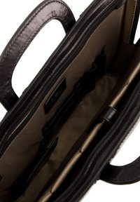 Indvendigt på en sort læderhandbag med en glat tekstur, prydet med en tan-farvet foer, flere lommer og en lynlåslukning. Håndtagene er synlige.