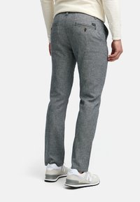Graue, strukturierte Hose mit schlanker Passform und Gesäßtaschen. Getragen mit hellgrauen Sneakers, die weiße Akzente und ein Markenlogo aufweisen.