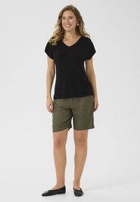 T-shirt noir à col en V et à manches courtes, associé à un short vert olive avec poches latérales et une coupe décontractée. Porté avec des ballerines noires.