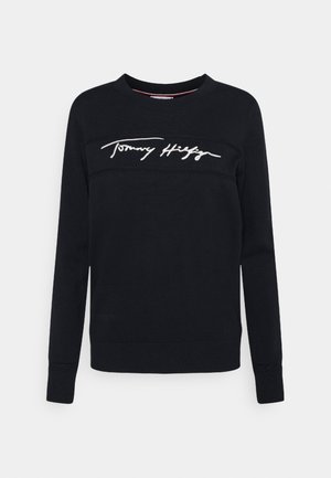 Sudadera negra hecha de tela con cuello redondo. Presenta texto bordado en blanco "Tommy Hilfiger" en el pecho y puños acanalados.