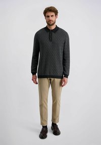 Schwarz- und graugemustertes langärmliges Poloshirt mit Kragen und einer Drei-Knopf-Leiste, kombiniert mit beigen Hosen und dunklen Schuhen.