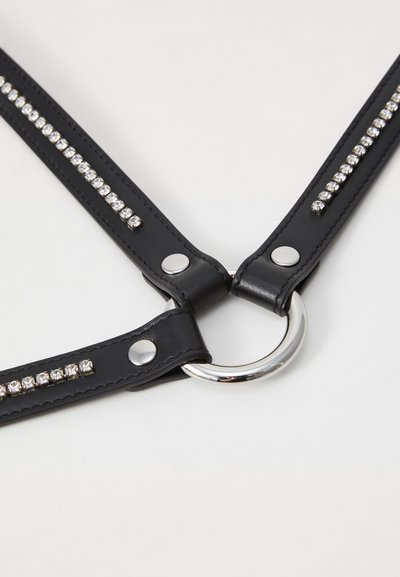 Čierny syntetický kožený postroj s krystalovými akcentmi, obsahujúci kruhový kovový krúžok a zacvakávaciu sponu, s pretínajúcimi sa popruhmi pre nastaviteľné prispôsobenie.