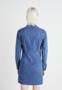 Τζιν φορεμα με μακριά μανίκια, κομμένη εφαρμογή και ορατές ραφές. Ανοιχτό μπλε χρώμα με λεία υφή, διαθέτει γιακά και κουμπωτά μανίκια.