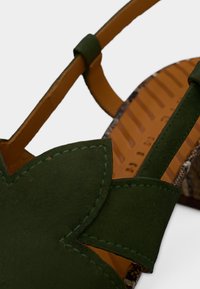 Sandale en daim vert avec un motif floral sur le dessus, dotée de lanières en cuir marron et d'une semelle intérieure texturée beige. Semelle extérieure en caoutchouc visible.