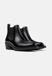 Botas de cuero negro hasta el tobillo con paneles laterales elásticos, un leve tacón en cuña, puntera redonda y textura suave. Diseño minimalista sin herrajes visibles.