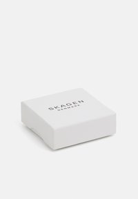 Confezione quadrata bianca con una texture liscia, che mostra la scritta "SKAGEN DENMARK" in lettere argento nella parte superiore. Design semplice e minimalista.