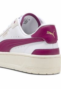 Zapatilla blanca con una franja lateral y talón de un rosa intenso brillante, detalle del logo en dorado, acabado de piel texturizada y suela de goma.