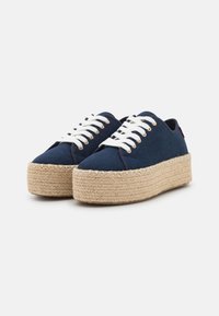 Navy canvas sneakers with white laces and metallic eyelets, featuring a tan espadrille-style jute platform sole.