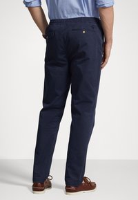 Marinblå chinos med elastisk midja och bakfickor, med detaljer i guldfärg. Slät bomullstyg med raka ben.