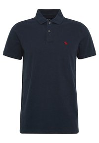 Námořnická modrá polo košile s krátkým rukávem, se dvěma knoflíky a malým červeným vyšitým logem losa na levé straně hrudi.