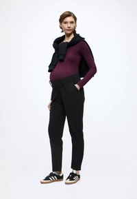 Conjunto premamá que incluye una camiseta ajustada de manga larga en color granate, pantalones negros de cintura alta y zapatillas negras con franjas blancas y beige.