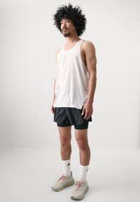 White mesh tank top with small perforations, paired with black shorts and light gray sneakers. White athletic socks with logo accents.