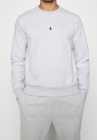 Sudadera gris hecha de una mezcla de algodón, con cuello redondo y mangas largas. Tiene un pequeño logotipo azul marino en el pecho.