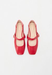 Zapatos planos de cuero rojo con un diseño de punta cuadrada, que cuentan con una banda ancha con un acento de hebilla dorada. El interior es beige con la marca.