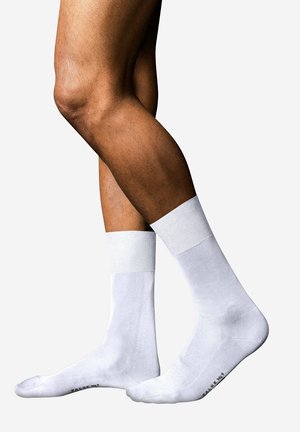 Two legs with medium brown skin wearing plain white crew socks against a white background, one foot slightly raised on toes.