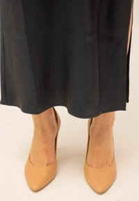 Scarpe con tacco alto beige con punta affusolata. Scarpe in pelle liscia, abbinate a un indumento scuro e fluido.