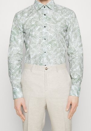 Langarmshirt van lichtgewicht stof met een groen palmenbladpatroon op een lichte achtergrond; gecombineerd met beige linnen broeken.