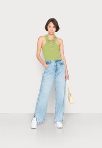 Top halter verde de riscas com detalhe de amarração, combinado com calças largas azuis claras com fendas laterais. Modelo segura uma pequena mala amarela.