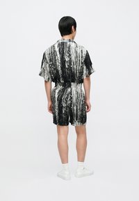 Schwarz-weiß gemusteter, abstrakter Jumpsuit mit kurzen Ärmeln und Gürtel, mit lockerem Schnitt und Seitentaschen, kombiniert mit weißen Turnschuhen.