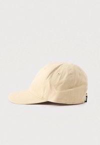 Beige pamut baseball sapka varrott szellőzőlyukakkal és ívelt világítással, bal oldalról, sima fehér háttér előtt bemutatva.