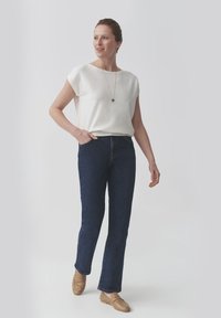 Valge lühikeste varrukatega shirt, tume teksariidest sirge lõikega teksad ja pruuni tooni libisevad jalanõud; lihtne disain puhta silueti ja minimaalsete aktsentidega.