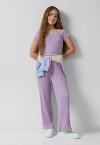 Ensemble en deux pièces en tricot côtelé lilas, comprenant un haut ajusté à manches courtes et un pantalon large, associé à un pull pastel noué à la taille.