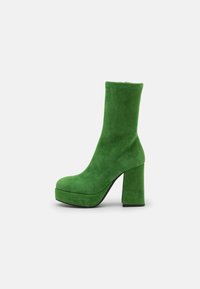 Bottines à plateforme en daim vert avec un haut talon bloc et un bout arrondi, présentant une construction sans couture et une texture lisse.