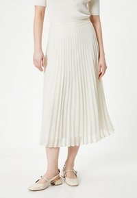 Gonna midi plissettata in crema chiaro con pois neri. Realizzata in tessuto testurizzato, presenta una vita aderente e un design fluente.