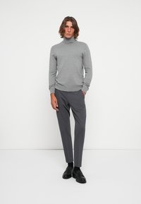 Siv turtleneck pulover in temno sivi hlače, ki imajo prilagojeno zasnovo in rebraste manšete. Črne čevlje dokončajo obleko.