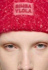 Czerwony dzianinowy beret o puszystej teksturze, z prostokątną różową metką z wytłoczonym napisem "BIMBA YLOLA" wszytą z przodu.