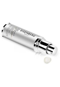 Flacon pompe cylindrique argenté avec une finition métallisée, arborant du texte noir et un bouchon en dôme transparent. Une petite goutte claire de produit se trouve à côté.
