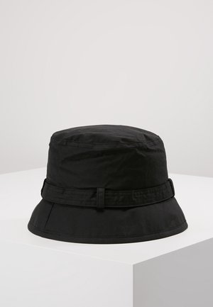 Czarna bucket hat z wąskim rondem i detalem z materiałowej taśmy wokół korony, umieszczona na białym piedestale na jednolitym tle.