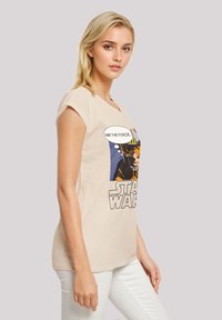 Beige graphic t-shirt featuring a comic-style design with "Star Wars" text and an illustration of a character. Short sleeves, relaxed fit.