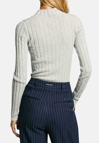 Svetlo siva rebrasta dolga majica z zaobljenim ovratnikom, kombinirana z mornarsko modrimi pritisnjenimi hlačami z zadaj žepi in podrobnostmi na pasu.