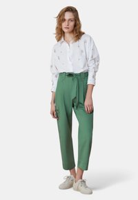 Camicia bianca con ricami floreali e pantaloni verdi con vita alta, dotati di cintura, tasche laterali e orli a risvolto. Sneakers bianche casual.